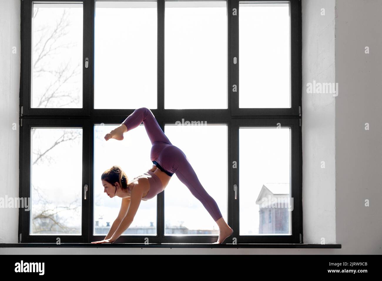 donna che fa esercizio di yoga sul davanzale della finestra in studio Foto Stock