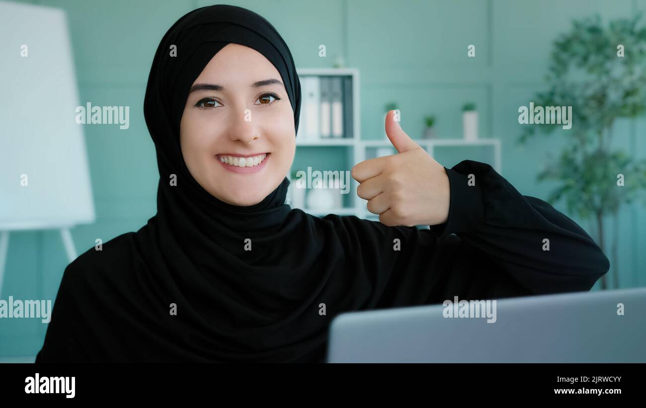 Arabo islamico musulmano studente in hijab nero riuscito businesswoman seduto al posto di lavoro home Office guardando il computer portatile schermo legge bene Foto Stock
