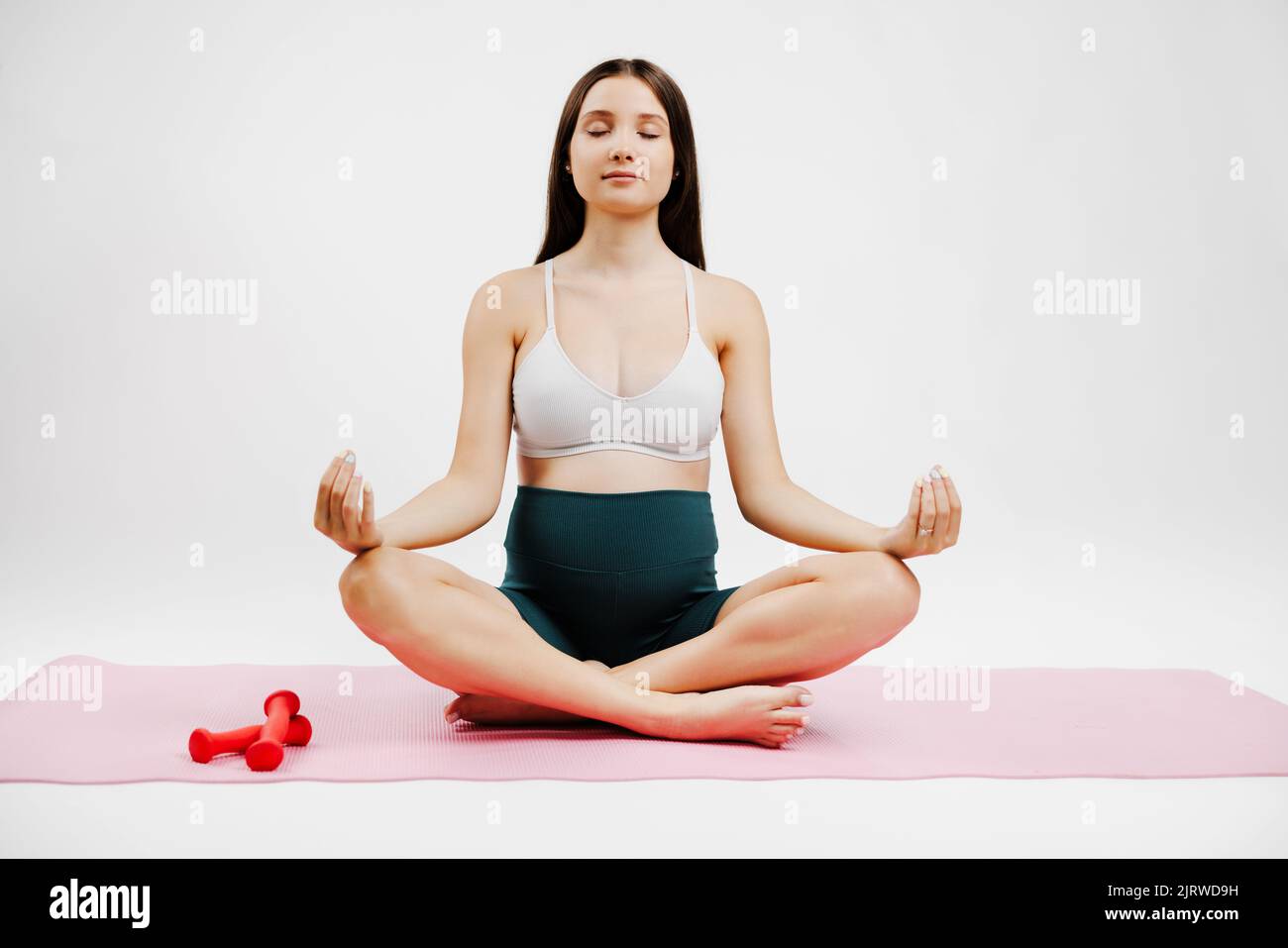 Giovane donna millenaria incinta seduta sul tappeto che esegue esercizi prenatali e di meditazione in una classe di yoga - concetto di vita e maternità Foto Stock