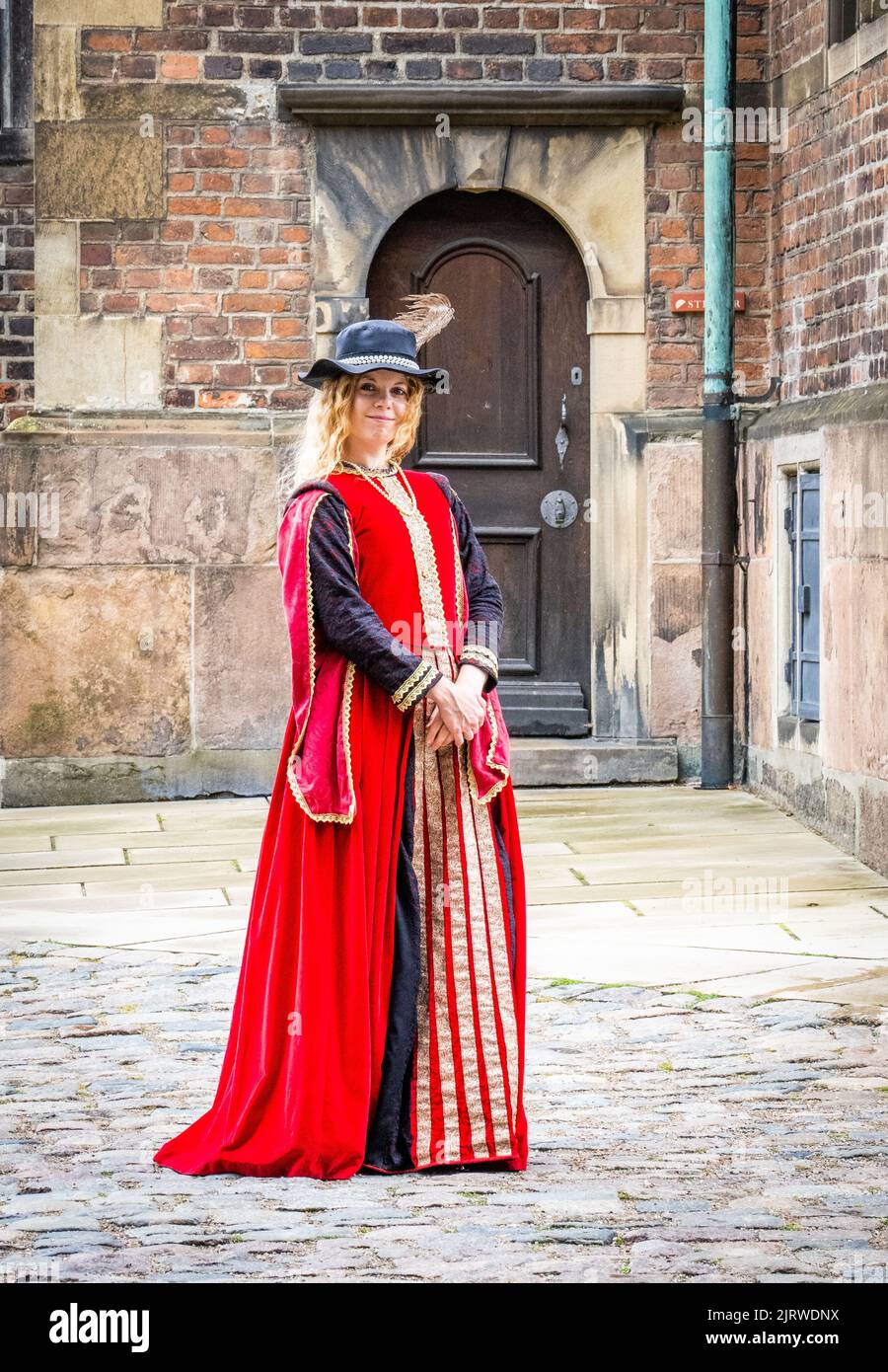 Giovane donna sorridente in abiti scarlatto e cappello di piuma che accoglie i visitatori alla Rosenborg slot costruita da Christian IV a Copenaghen in Danimarca Foto Stock