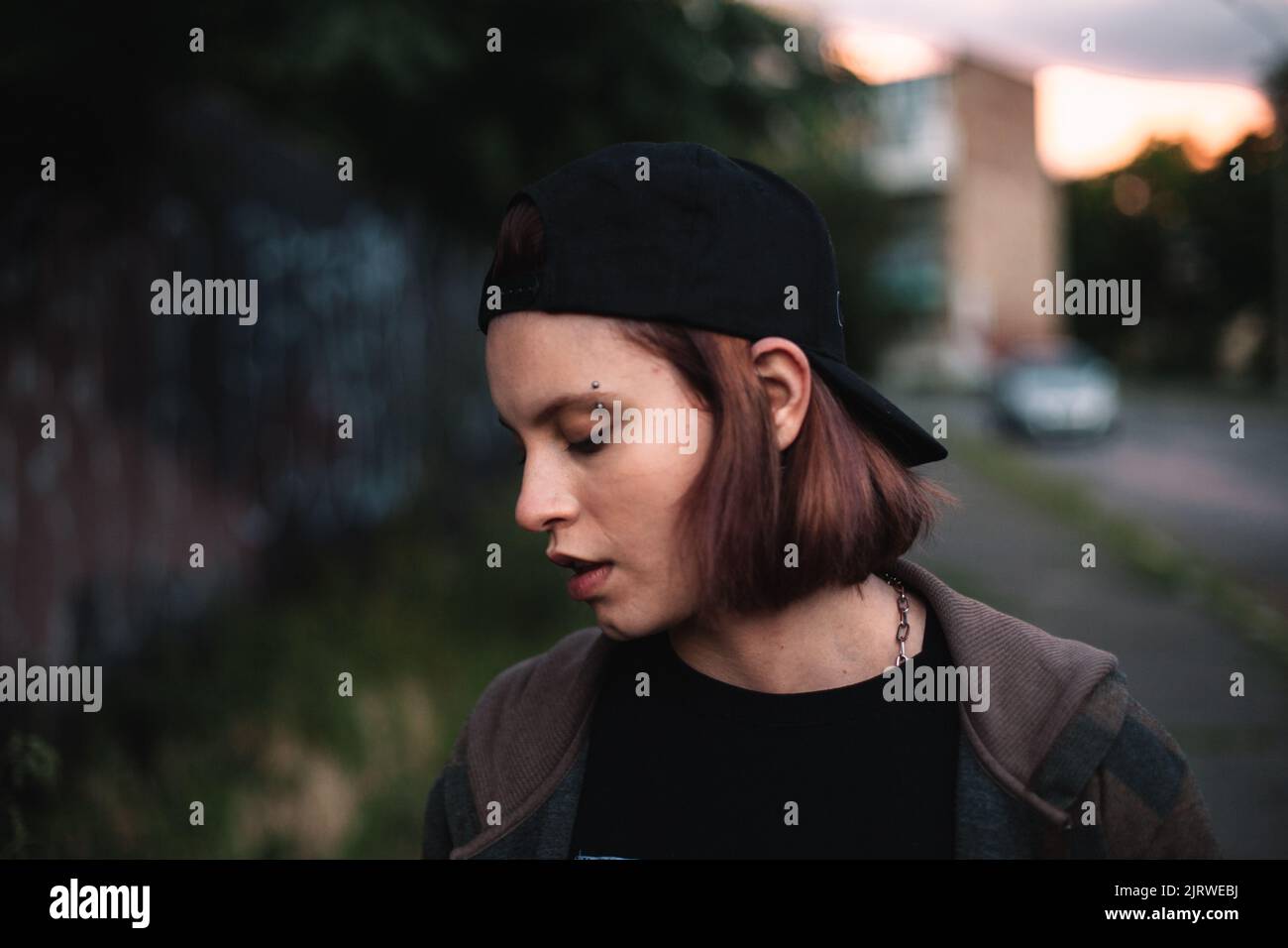 Giovane donna punk con sopracciglia trafitto che indossa il cappuccio all'indietro all'aperto Foto Stock