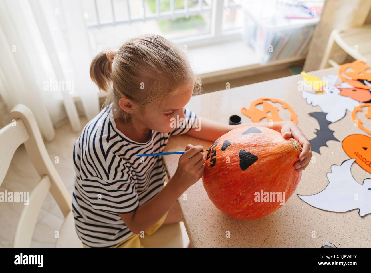 Una ragazza dipinge una zucca con pitture per Halloween. Foto Stock