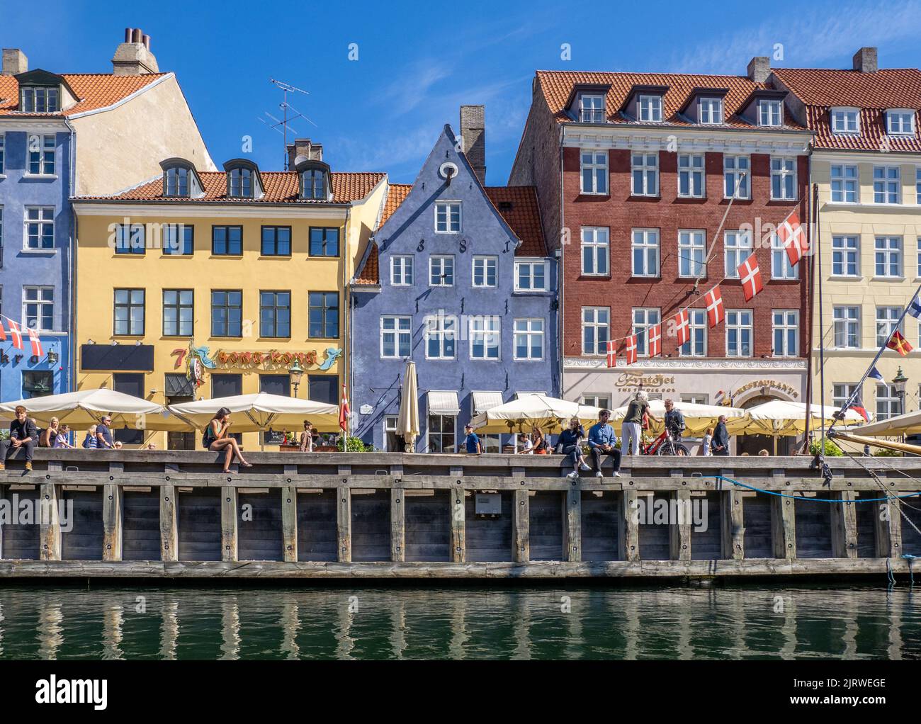 Rilassatevi al sole presso la popolare destinazione turistica di Nyhavn, un canale fiancheggiato da colorate case a 17th C, caffè e bar - Copenhagen Danimarca Foto Stock