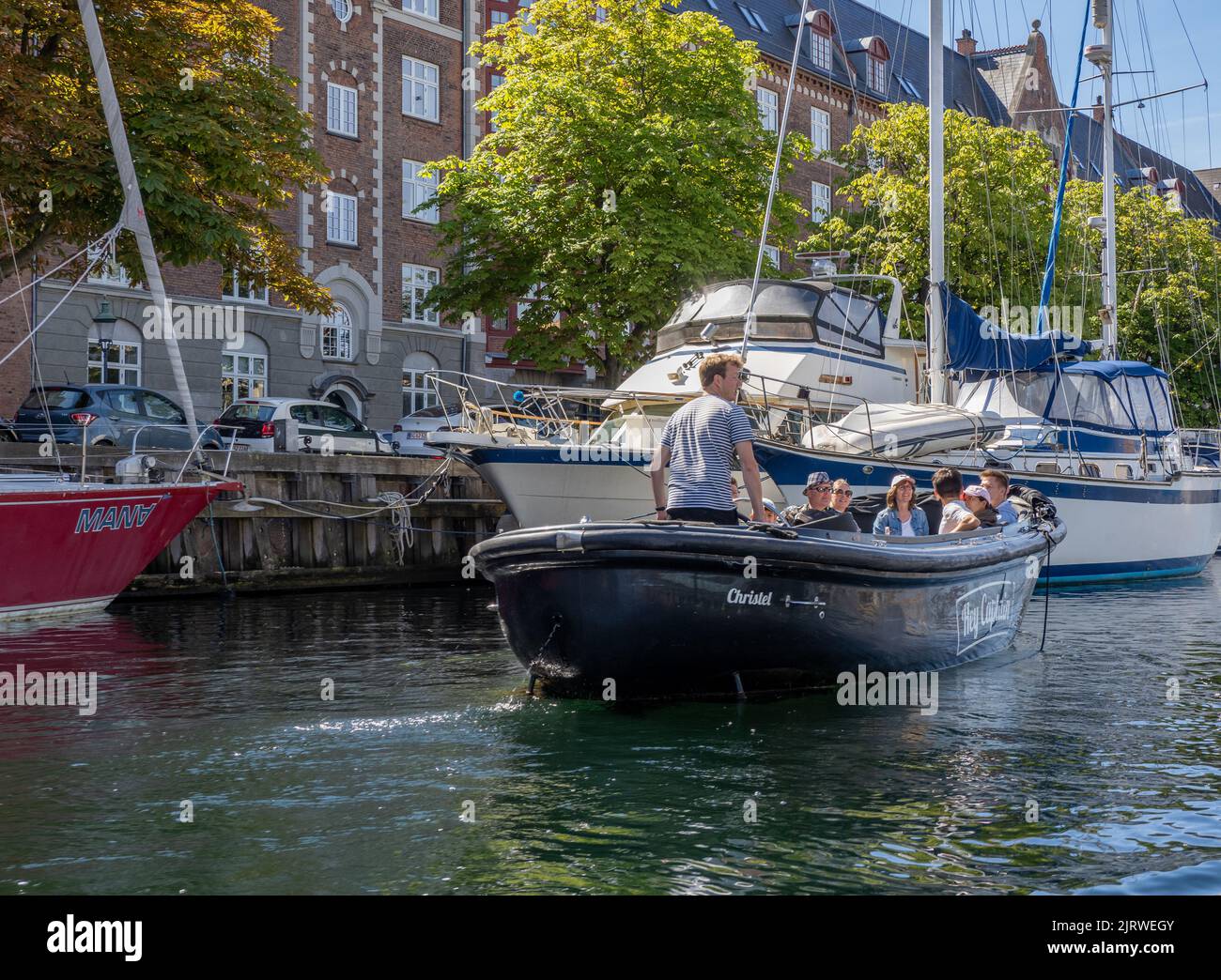 I turisti si godono un piccolo tour guidato in barca di Copenhagen, Danimarca, su una barca che naviga lungo uno dei canali della città sotto il sole luminoso Foto Stock