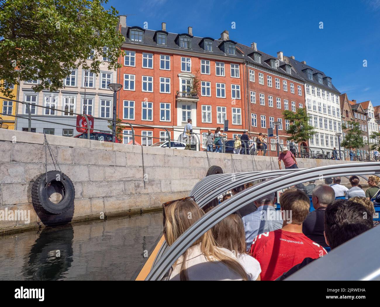 I turisti che si godono un tour guidato di Copenhagen, Danimarca, su una barca a vela lungo il Frederiksholms Kanal sotto il sole luminoso Foto Stock