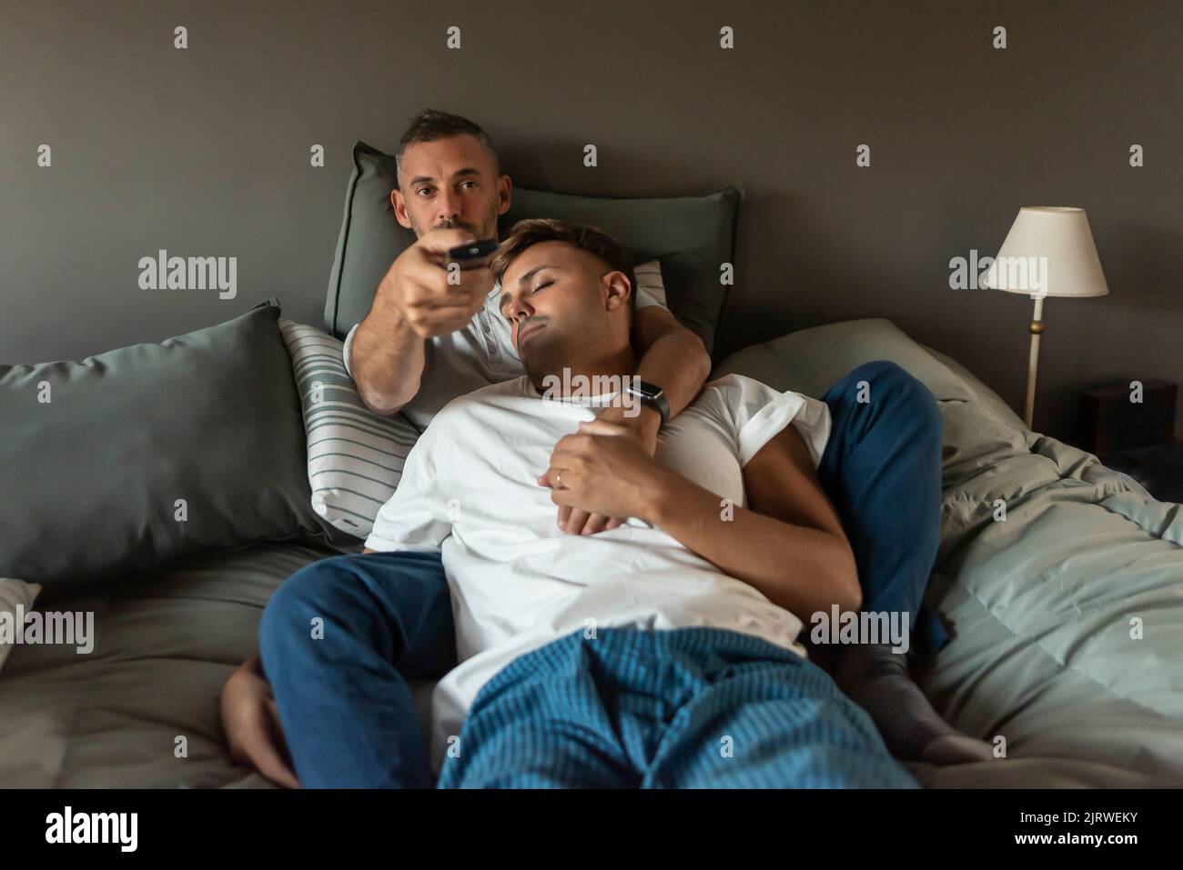 Coppia gay maschio a letto. Uno guarda la tv mentre l'altro dorme Foto Stock