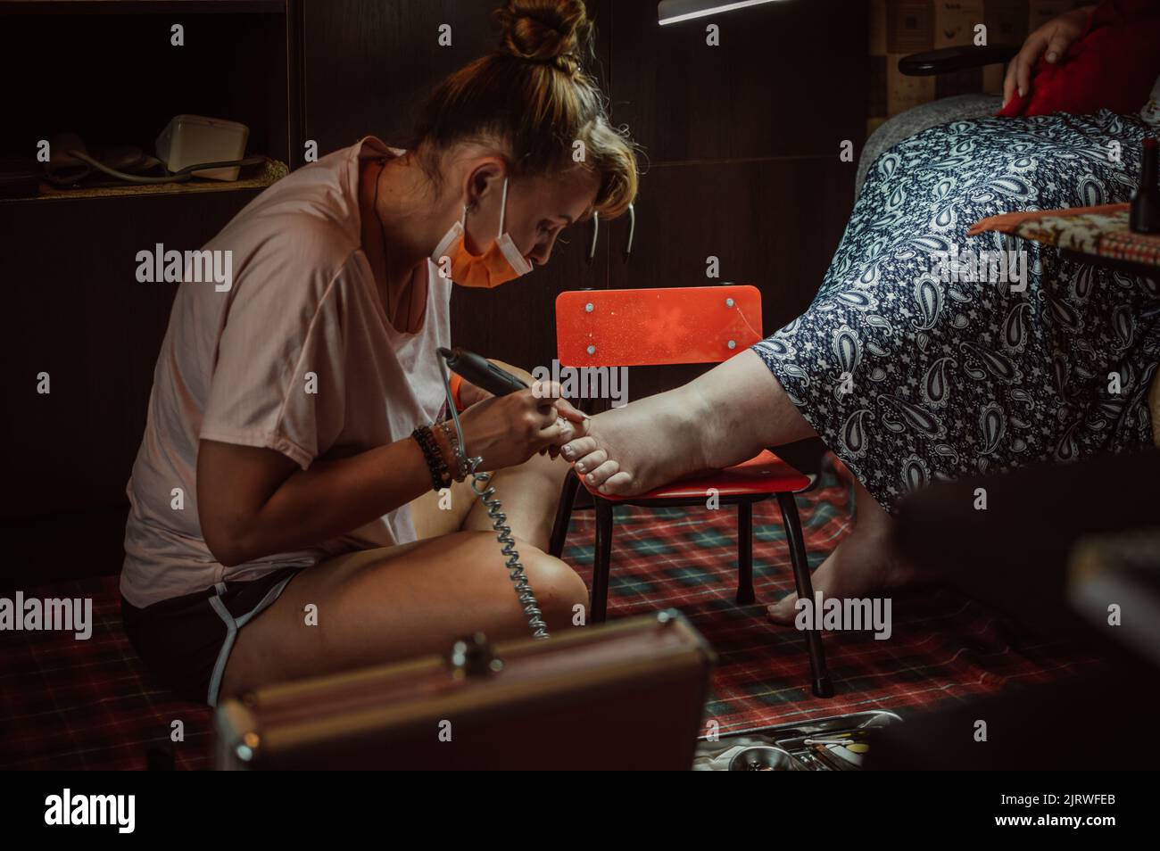 Pedicurista mascherato fa pedicure a casa per più donna formato Foto Stock