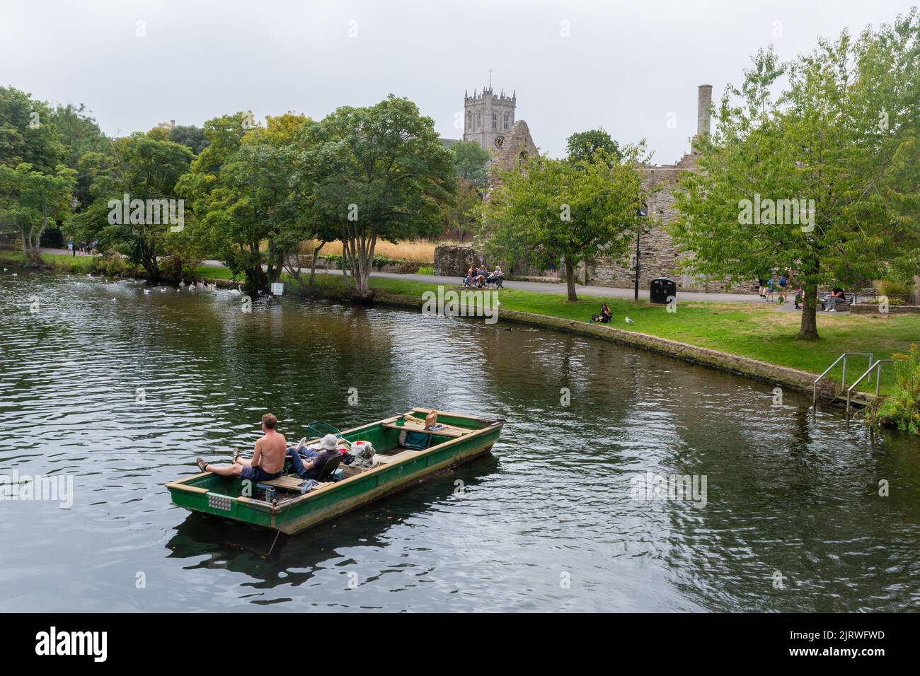 Due uomini che pescano da una barca sul fiume Avon vicino al Priorato di Christchurch e la Norman House, un castello in rovina tenere, Christchurch Dorset, Inghilterra UK Foto Stock