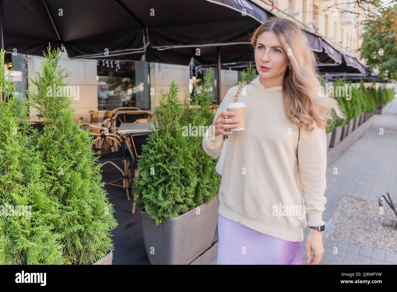 La ragazza sta andando sulla strada con tazza di caffè artigianale Foto Stock