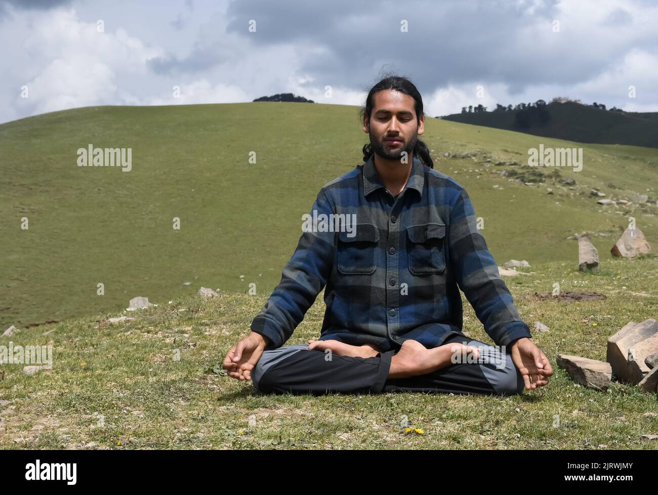 Vista frontale di un giovane indiano che pratica yoga in posa Lotus (Padmasana) con Gyan Mudra (Gesture of Knowledge) in montagna. Foto Stock