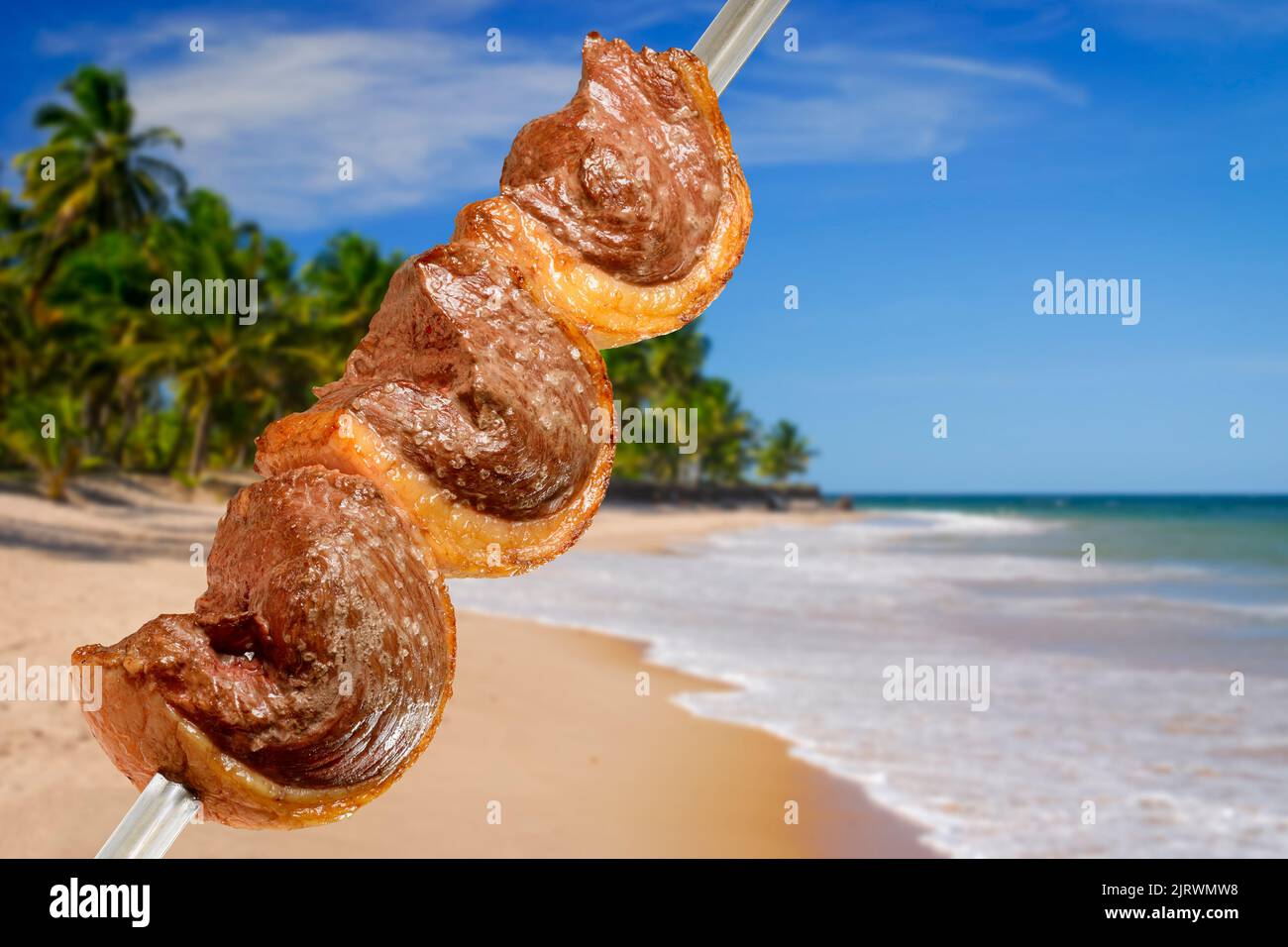 Barbecue picanha grigliato su spiedini con scena brasiliana sulla spiaggia sullo sfondo. Foto Stock