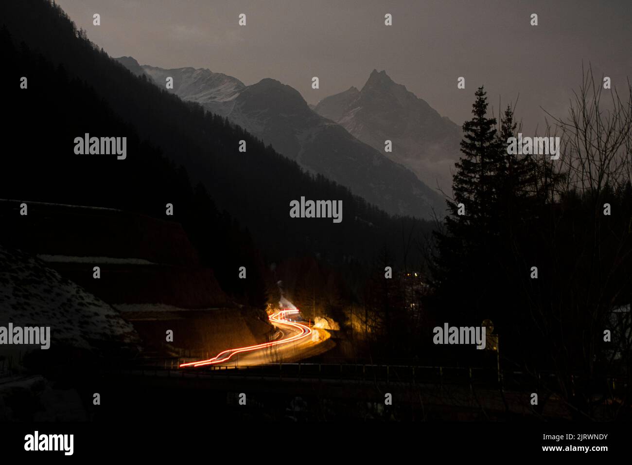 Le auto guidano fino a una strada di montagna ventosa di notte, con una lunga esposizione che mostra una leggera traccia di fari Foto Stock