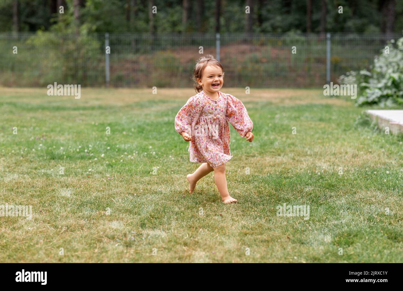 ragazza piccola felice che corre a piedi nudi sull'erba Foto Stock