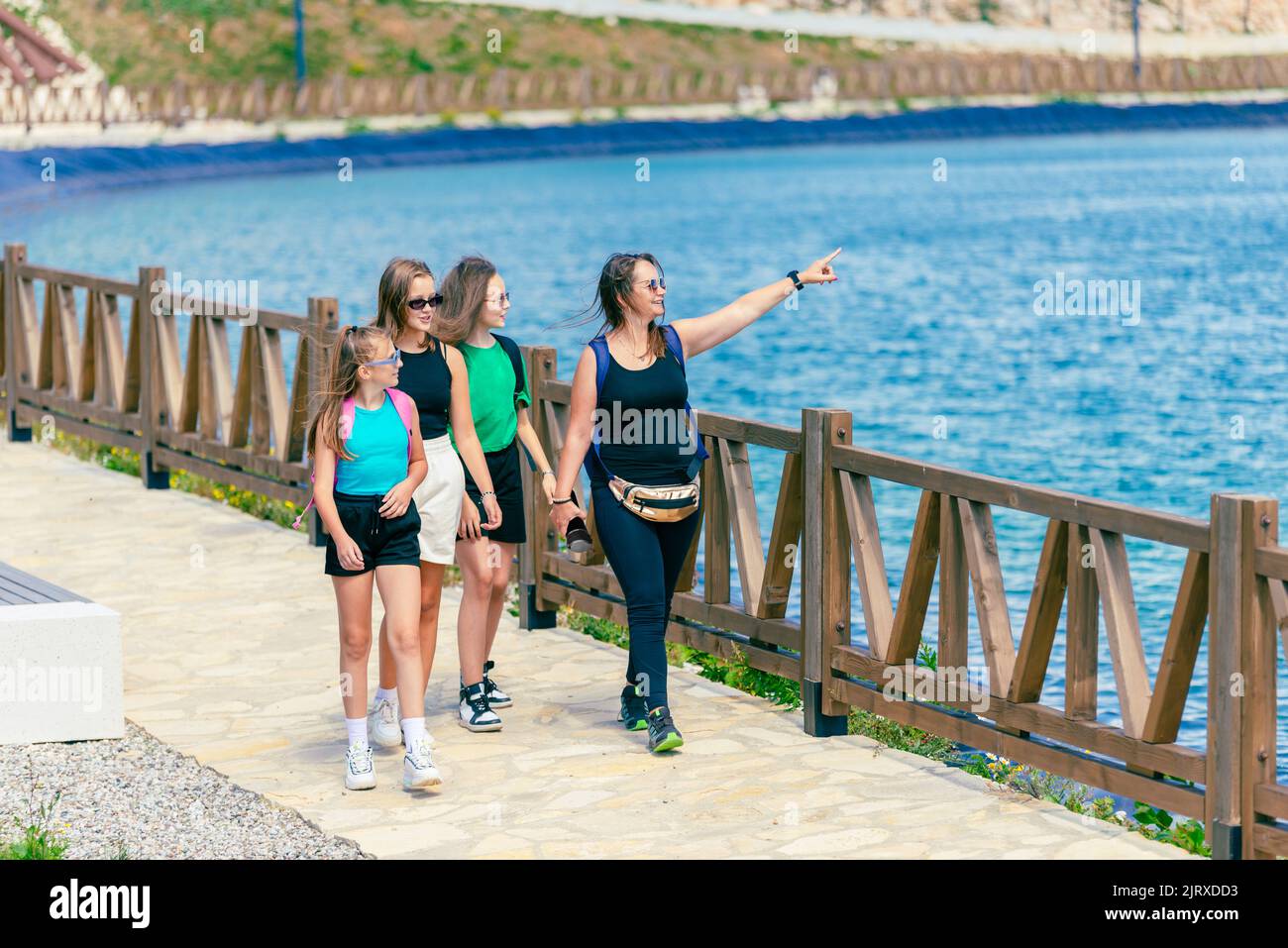 Le ragazze e una donna stanno camminando vicino al lago. La donna mostra alle ragazze un'attrazione turistica. Concetto di turismo di montagna e divertimento Foto Stock