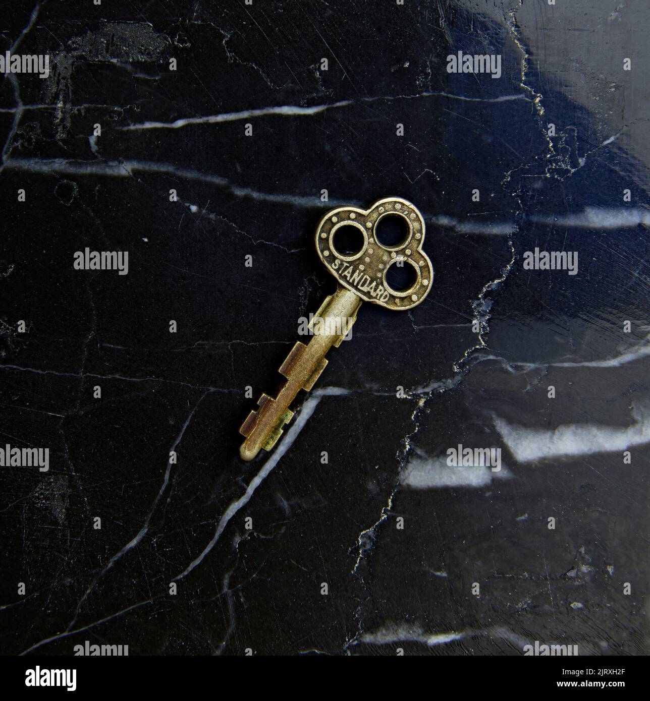 Primo piano di una piccola chiave decorativa antica. Su sfondo di marmo nero. Foto Stock