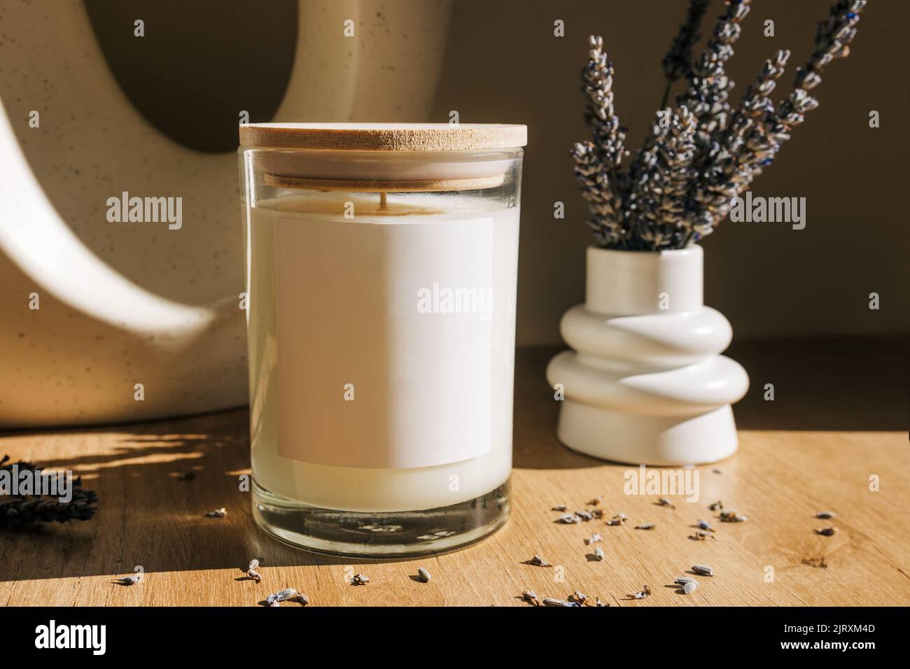 Candela di cera naturale con etichetta vuota e vaso piccolo con fiori di lavanda. Etichetta candela mock-up. Luce naturale, foto lifestyle Foto Stock