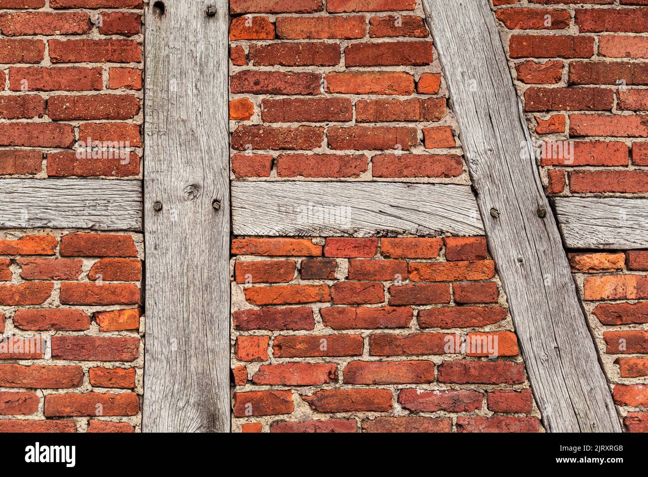 Trama di fondo di una vecchia parete in legno, costituita da travi in legno intemperie e mattoni rossi di bakestone, tipico per architettura a graticcio Foto Stock