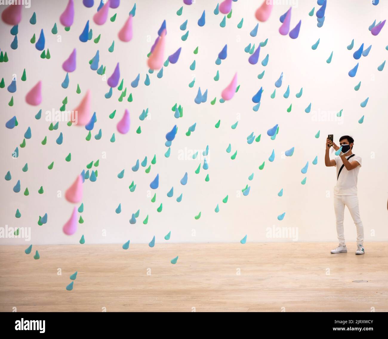 L'uomo che indossa la maschera facciale scatta una foto da smartphone dell'installazione artistica di arcobaleni colorati dell'artista svizzero Urs Fischer nel Museo Jumex, Città del Messico, Mex Foto Stock