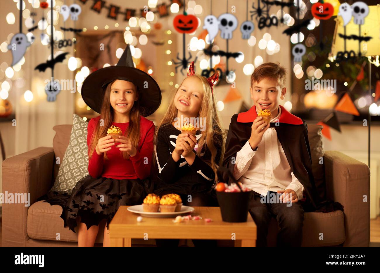 bambini in costumi di halloween mangiare cupcakes a casa Foto Stock