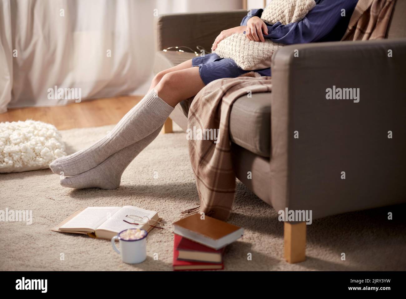 donna in calze con cuscino e libri a casa Foto Stock