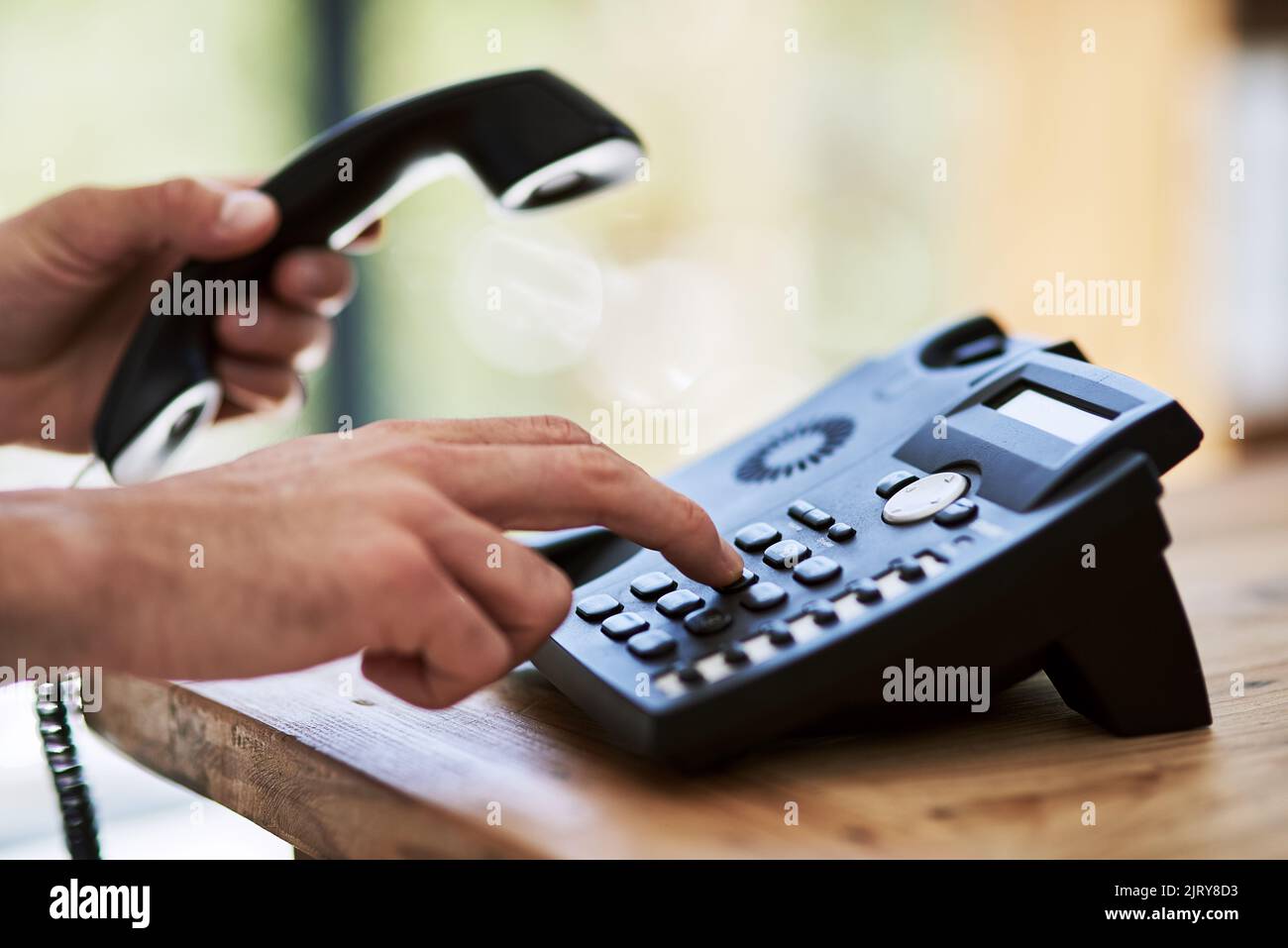 Effettuare la chiamata e farlo avvenire. Un uomo che compone un numero su un telefono al lavoro. Foto Stock