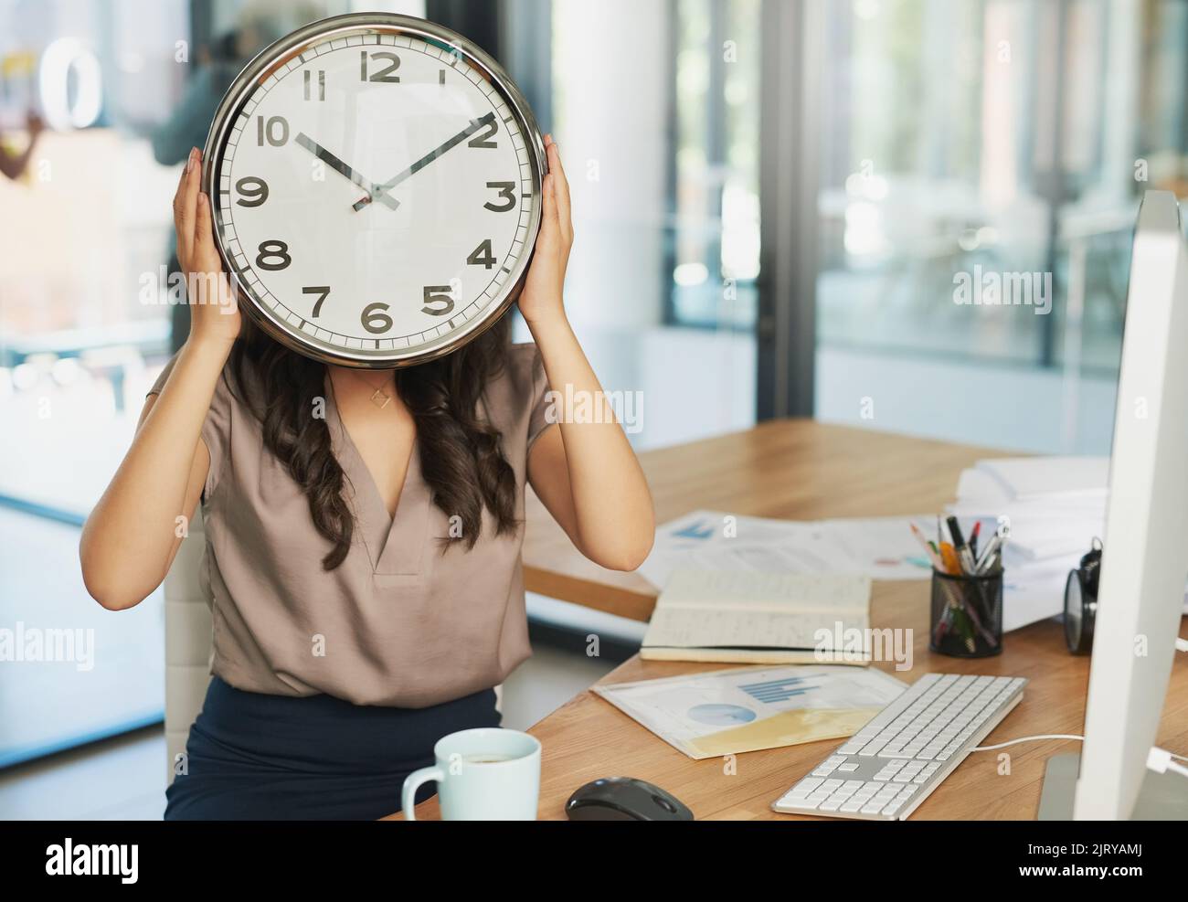 Tick tock, tick tock. Una donna d'affari non identificabile che tiene un orologio davanti al viso mentre si siede alla scrivania. Foto Stock