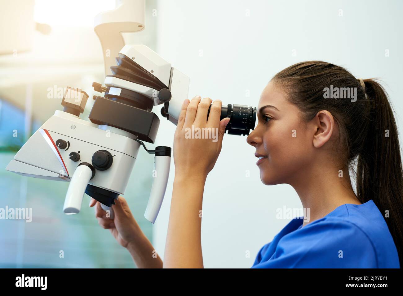 Conoscere la sua paziente a livello molecolare, un giovane patologo che guarda i campioni al microscopio. Foto Stock