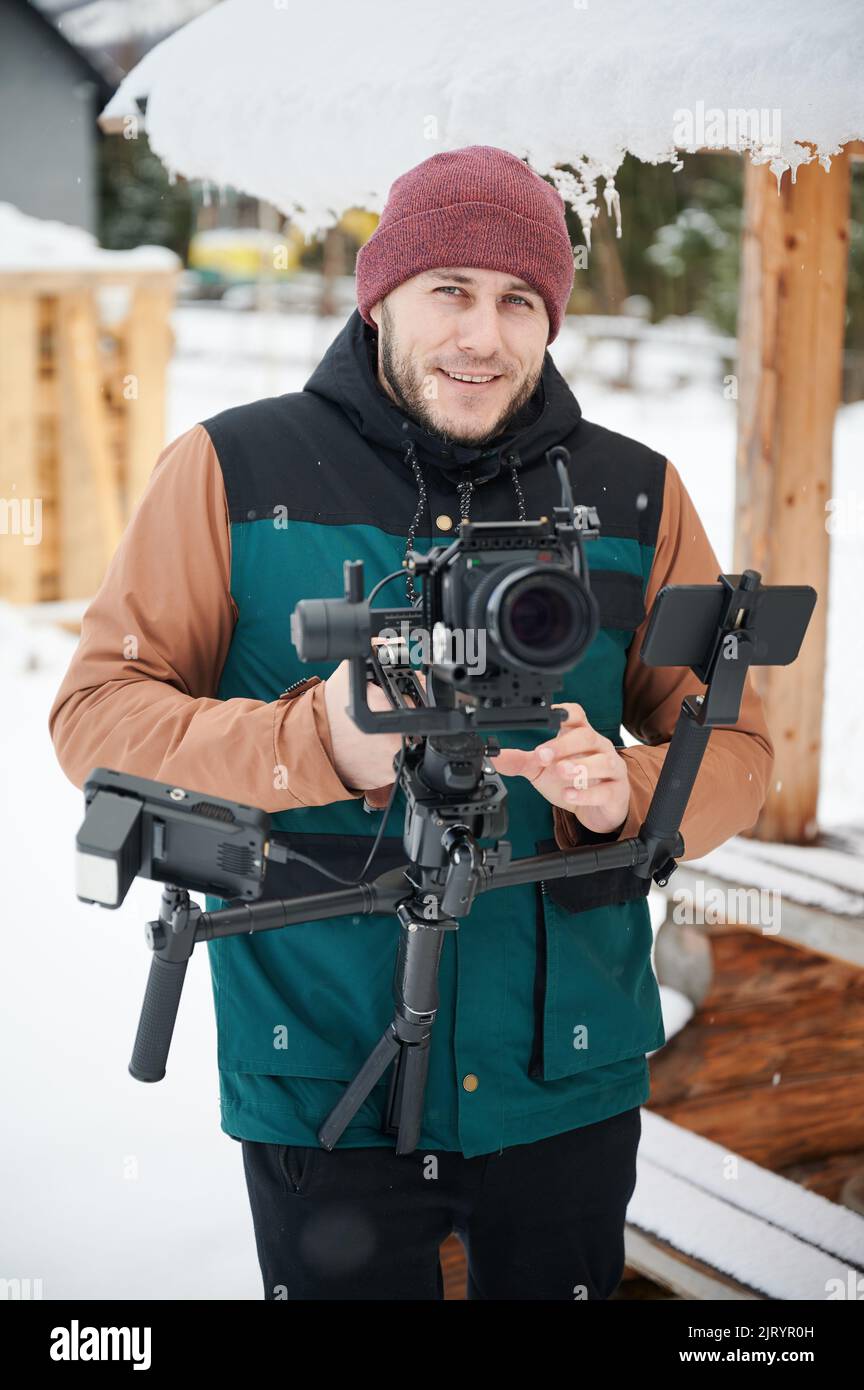 Ritratto di uomo felice videografo che scatta riprese, utilizzando la fotocamera montata su un equipaggiamento stabilizzatore di gimbal in inverno. Foto Stock