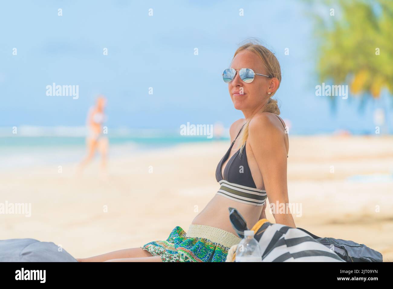 donna bionda che si rilassa sulla spiaggia tropicale con occhiali da sole in bikini Foto Stock