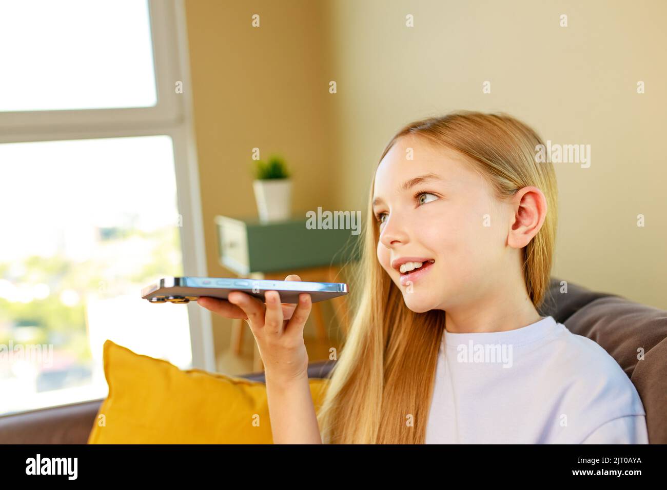 Felice ragazza adolescente t-shirt in cotone seduto sul divano a casa registrazione messaggio vocale Foto Stock