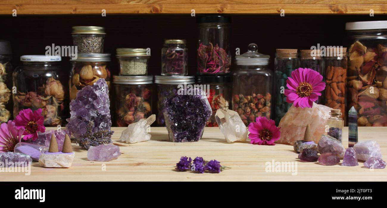 Cristalli di Ametista e fiori sulla Tabella di meditazione con vasi di erbe essiccate in background Foto Stock