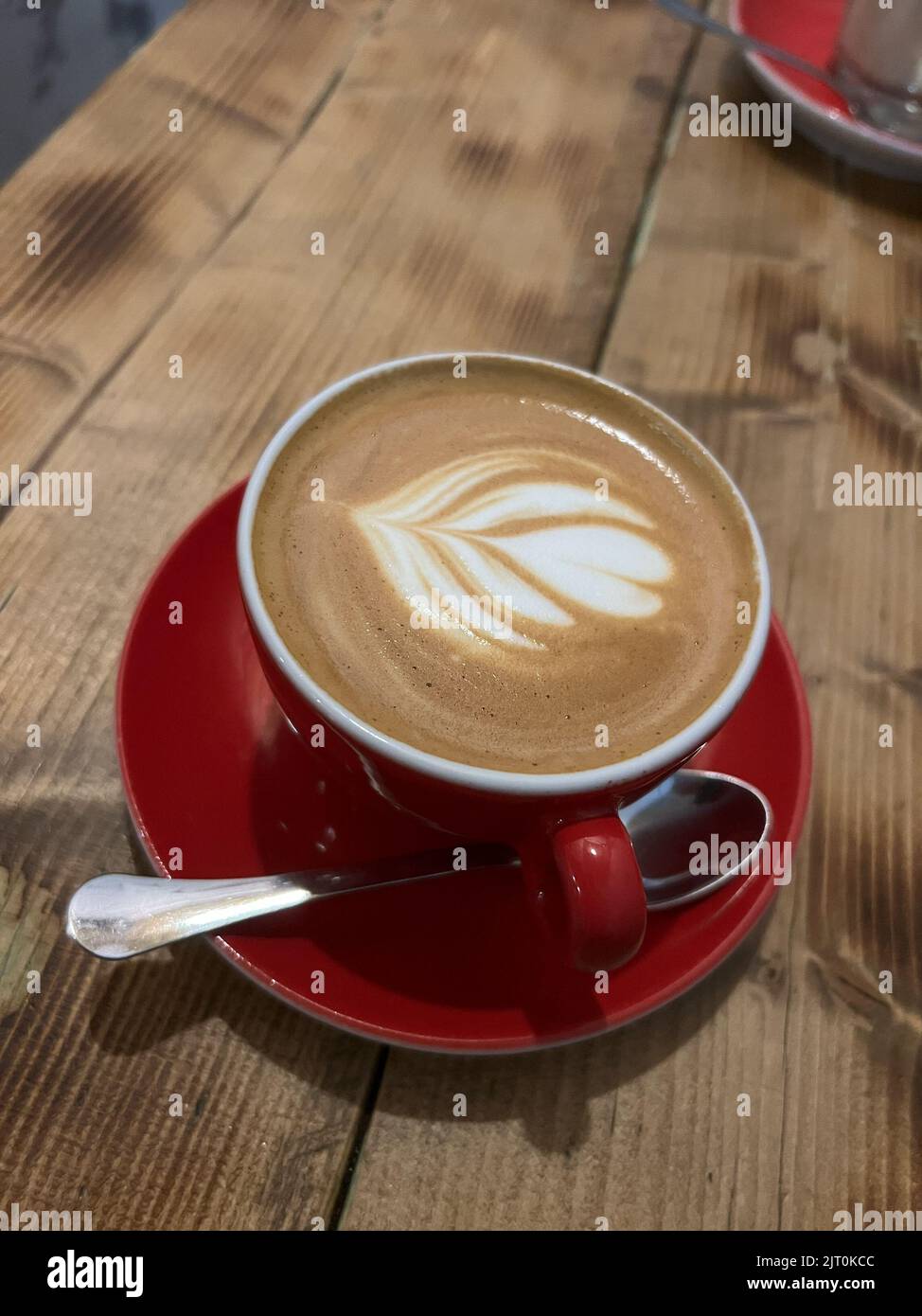 Caffè con un motivo in una tazza su un piattino rosso. Primo piano Foto Stock