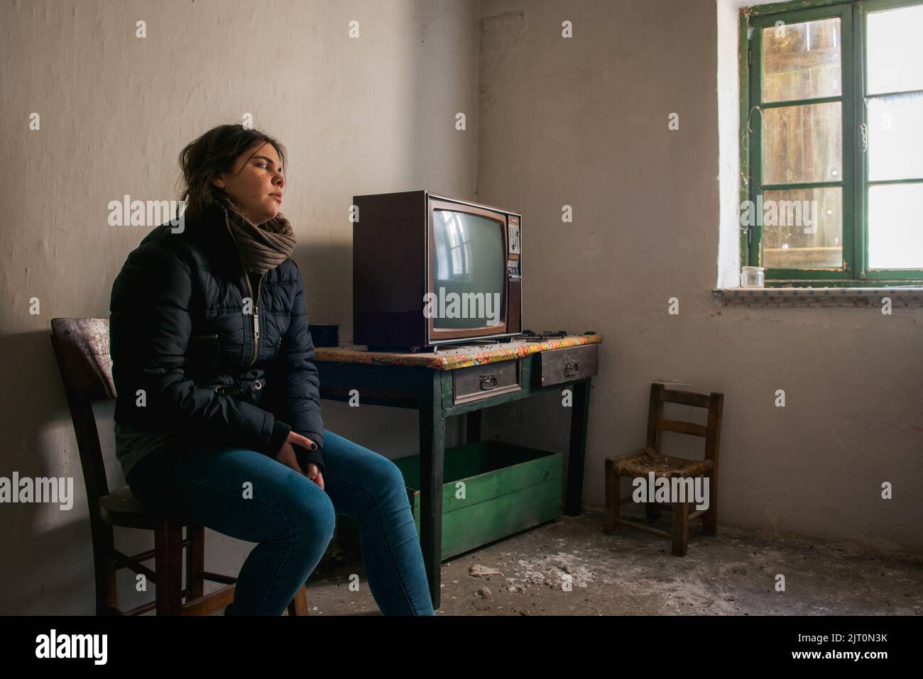 Giovane donna sola in una stanza abbandonata in rovina con televisione. Concetto di solitudine Foto Stock