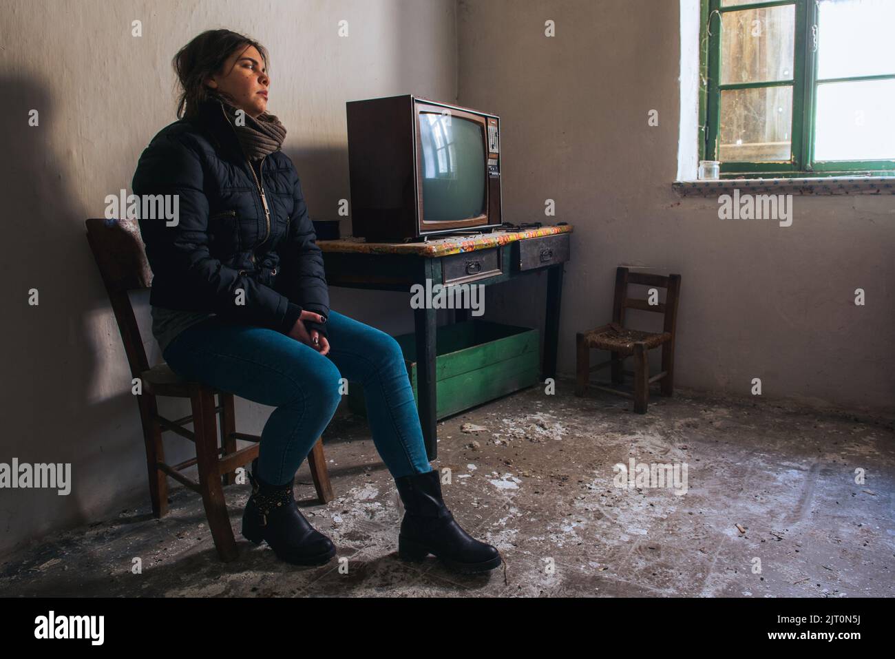 Giovane donna sola in una stanza abbandonata in rovina con televisione. Concetto di solitudine Foto Stock