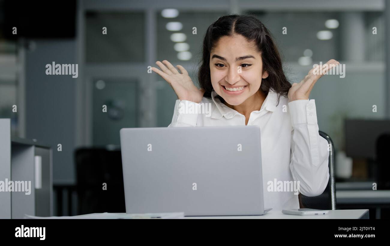 Giovane donna manager seduto in ufficio guardando lo schermo del notebook che riceve la notifica legge buone notizie gioisce nel successo celebrare la vittoria sente Foto Stock