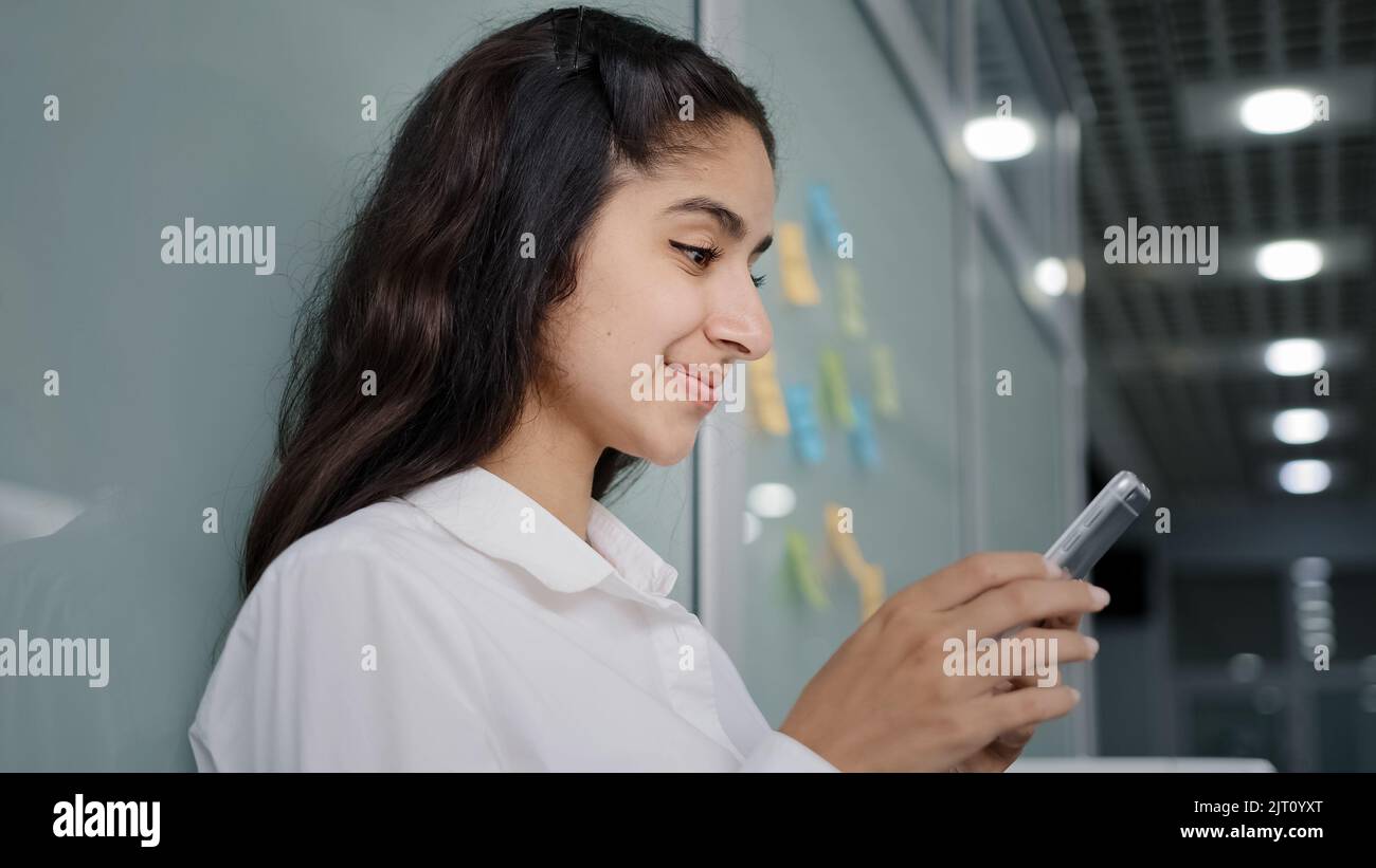 Vista laterale giovane donna sorridente che naviga sui social network effettua ordini nel negozio online utilizzando la comunicazione remota tramite smartphone in chat sul telefono Foto Stock