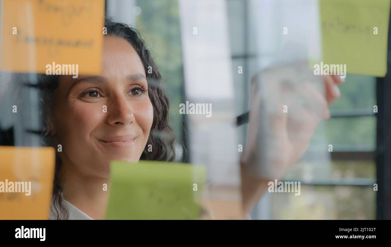 Giovane donna ispanica positivo lavoratore ufficio scrive compiti progetto su note appiccicose organizza piani di lavoro strategia di successo businesswoman sviluppa piano Foto Stock
