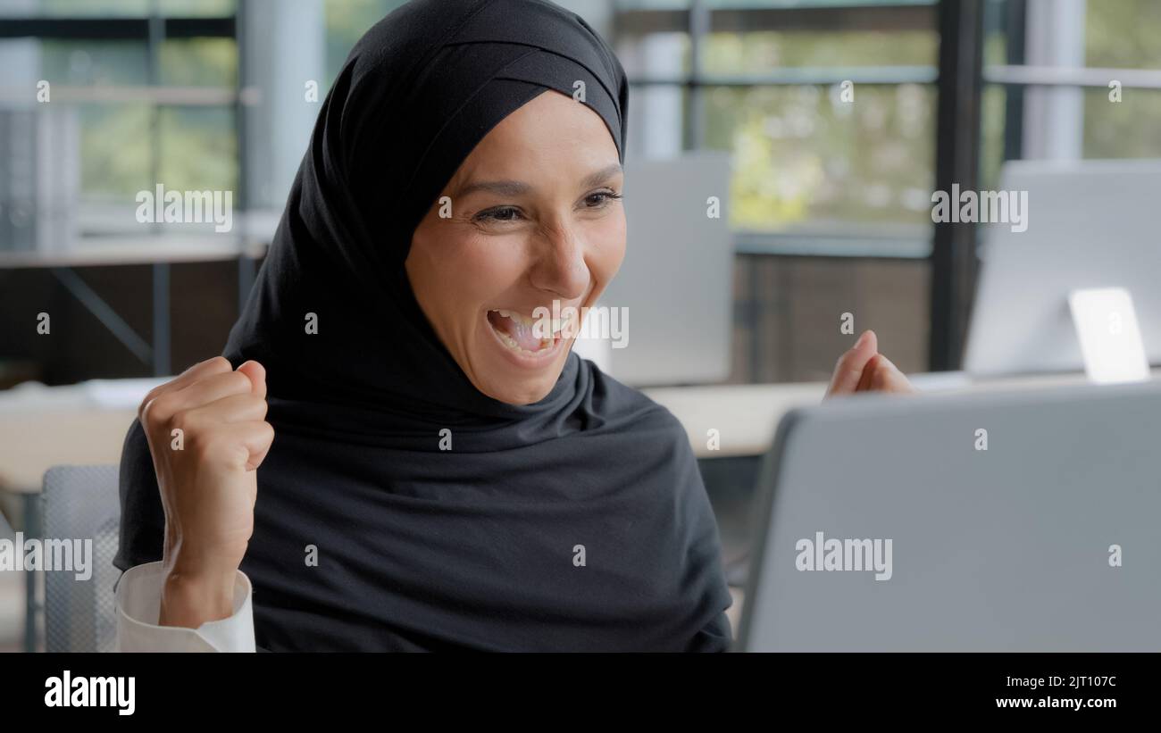 Giovane donna araba eccitata che controlla la posta elettronica sul portatile concentrazione leggere ottiene buone notizie stupito felice imprenditore vincitore celebrando la vittoria gioisce Foto Stock