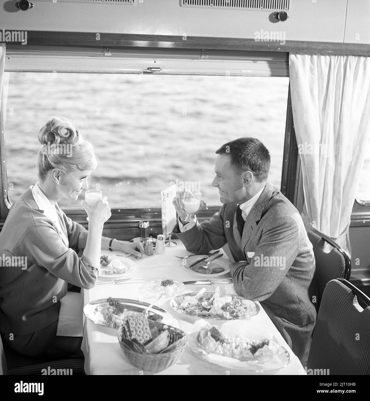 Viaggio in treno nel 1960s. Una coppia nella macchina del ristorante del treno sta godendo la cena insieme. Ha una tipica acconciatura 1960s. Svezia 1960s Kristoffersson Ref DD107-5 Foto Stock