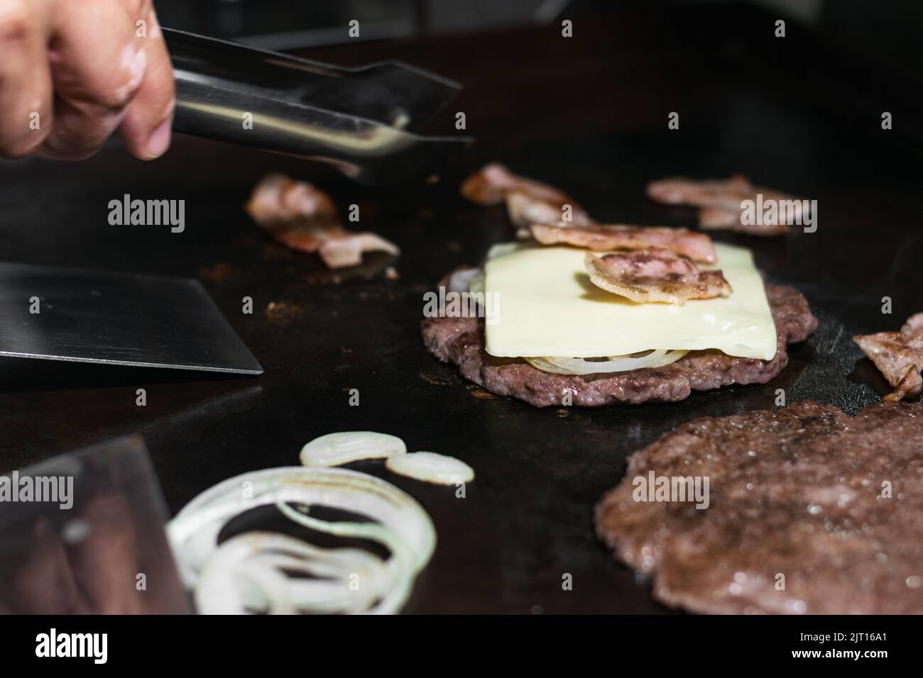 dettaglio primo piano di due polpettine di hamburger macinati con una fetta di mozzarella in cima, cipolle e pancetta intorno a loro, cottura Foto Stock