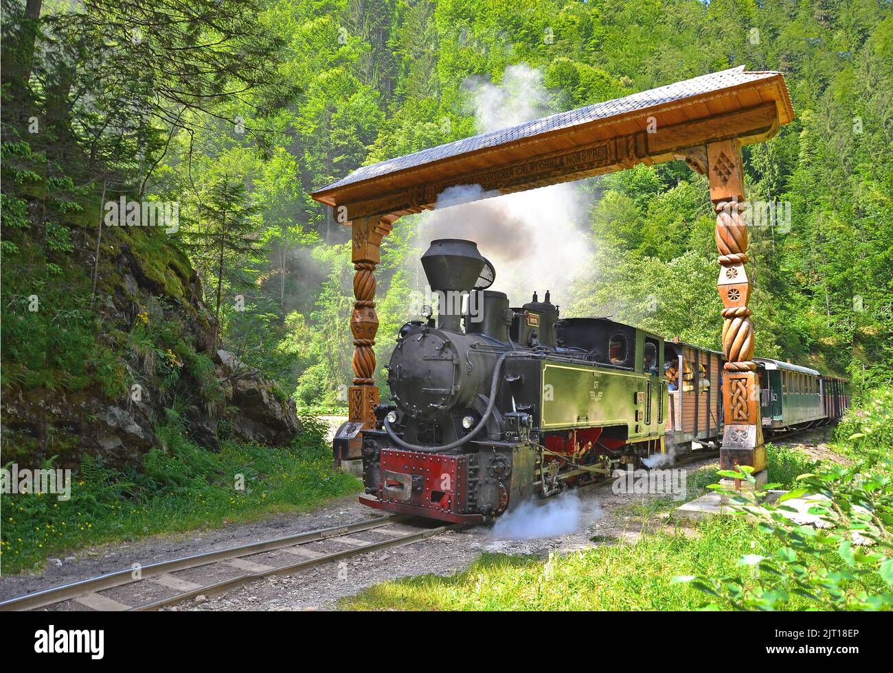 Un primo piano di un vecchio treno a vapore che passa sotto una porta di legno nella Valle di Vaser, Maramures, Romania Foto Stock