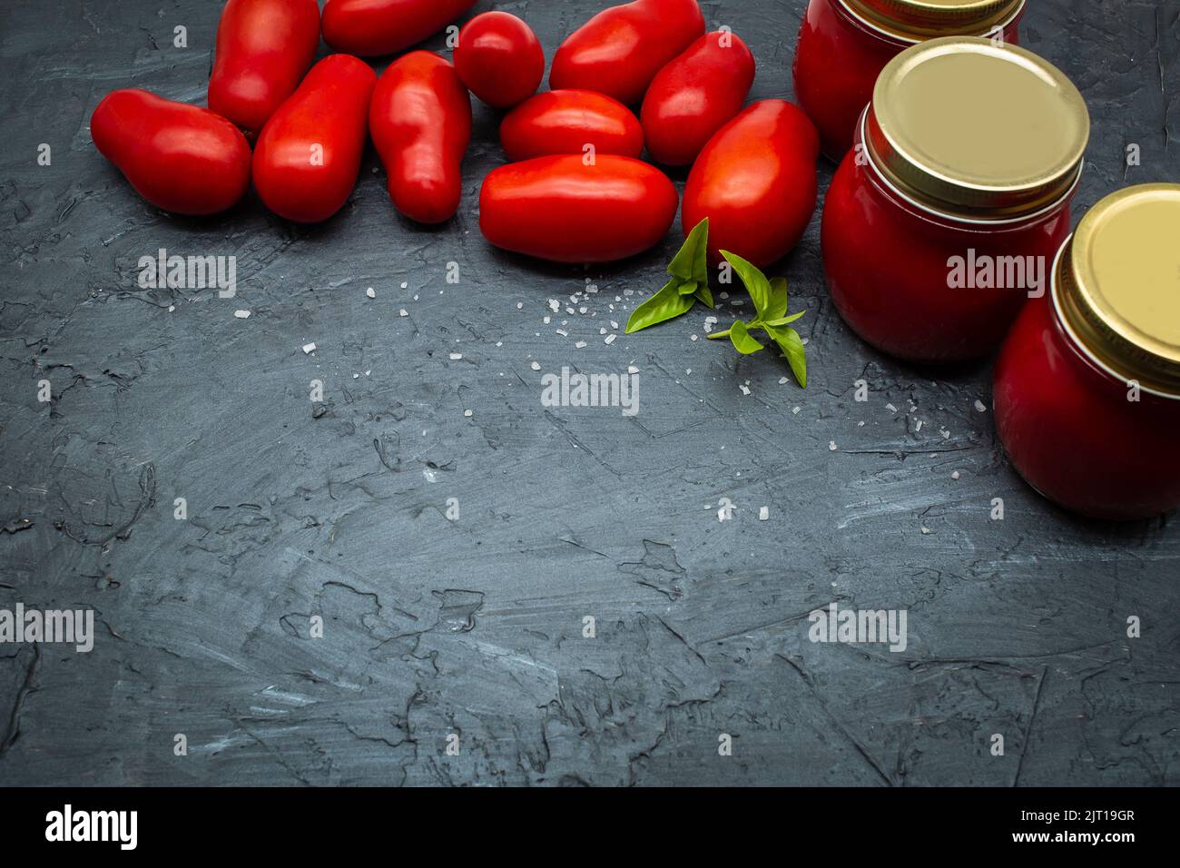 Vista dall'alto della tradizionale salsa di pomodoro italiana in un vasetto di vetro con pomodori freschi e basilico. Spazio di copia. Foto Stock