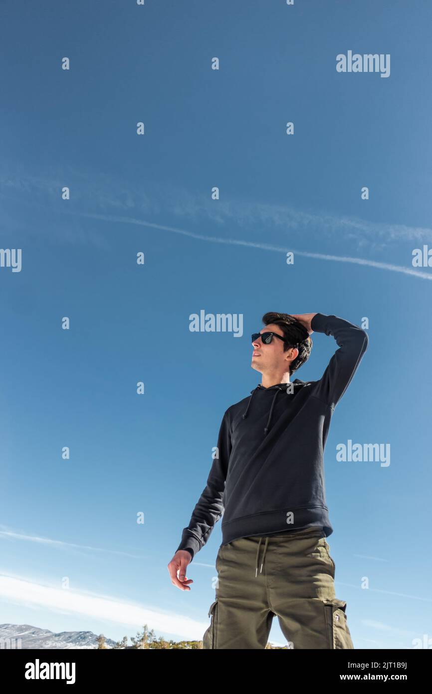 Bell'uomo caucasico che si presenta con il cielo blu sullo sfondo. Indossa un paio di occhiali da sole neri Foto Stock