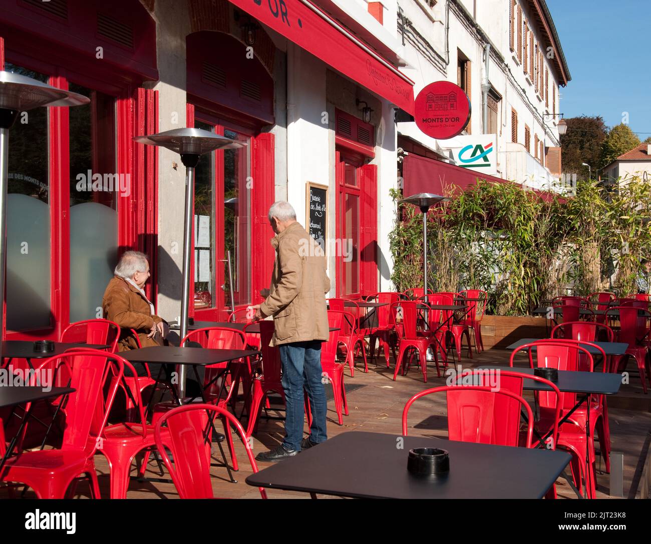 Bar sulla piazza principale, St Cyr au Mont d'Or, Lione, Auvergne-Rodano-Alpi, Francia. Due clienti chiacchierano dopo aver bevuto un caffè. Foto Stock