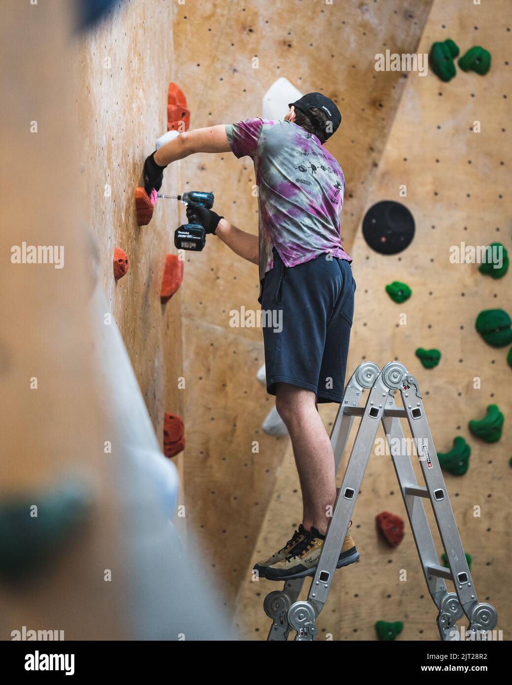 Un apparecchio di arrampicata che cerca di impostare un percorso nella palestra bouldering Foto Stock