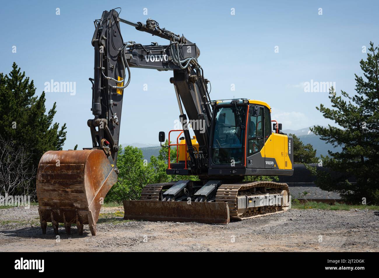 Un grande escavatore Volvo EC160E giallo e nero con una benna in un cantiere con alberi Foto Stock
