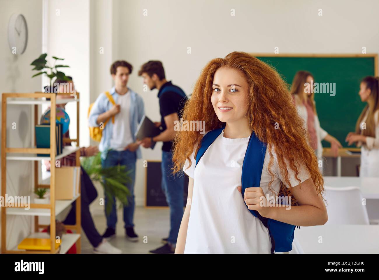 Bella ragazza carina con capelli rossi studente in classe sullo sfondo dei suoi compagni di classe Foto Stock