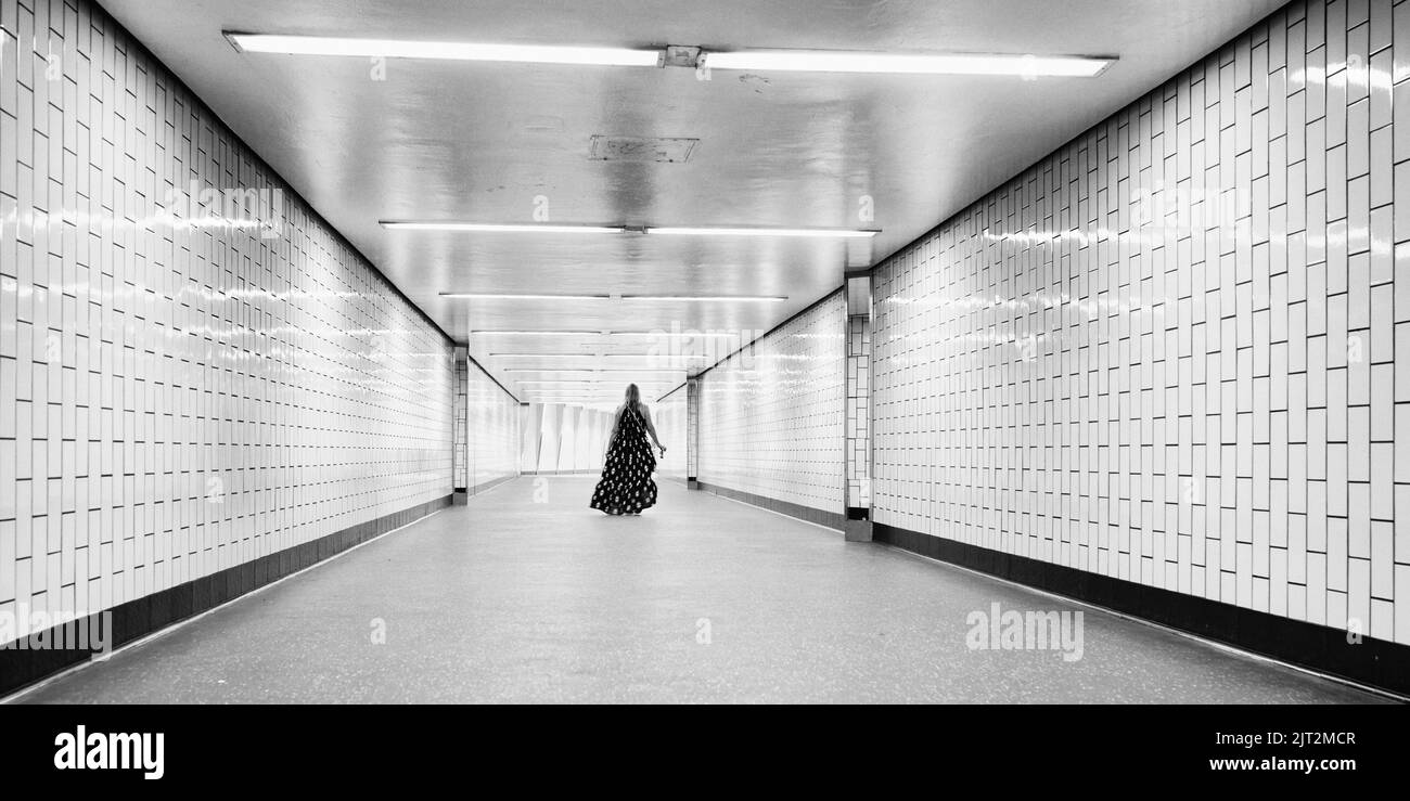 una donna in un vestito estivo cammina attraverso un passaggio solitario della metropolitana Foto Stock