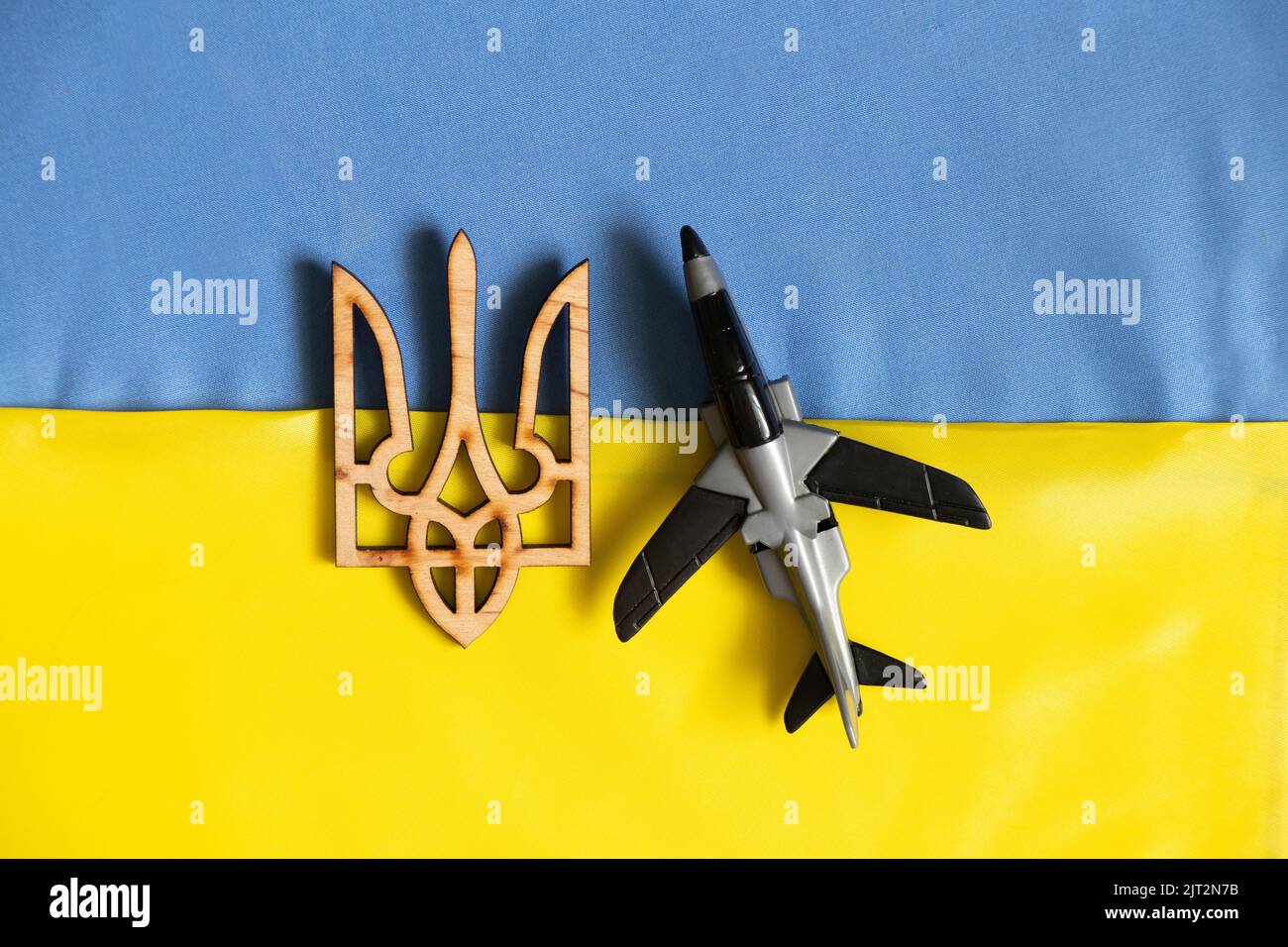 Un aereo giocattolo per bambini giace sulle bandiere nazionali dell'Ucraina e uno stemma di legno, la guerra in Ucraina, un cielo chiuso Foto Stock