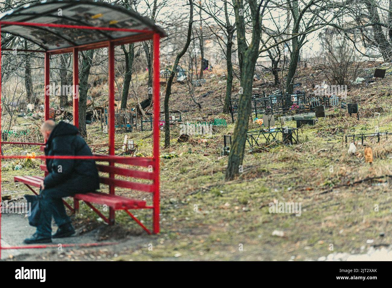 Un vecchio seduto nella stazione degli autobus sullo sfondo del cimitero Foto Stock